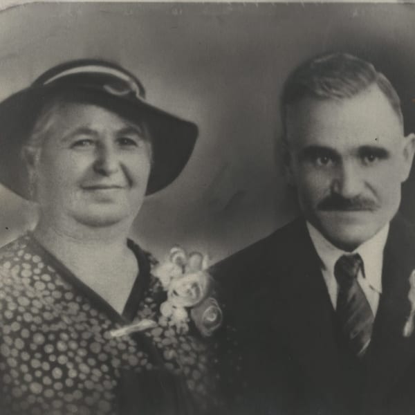 Black and white portrait of a smiling woman in a hat and a man in a suit.