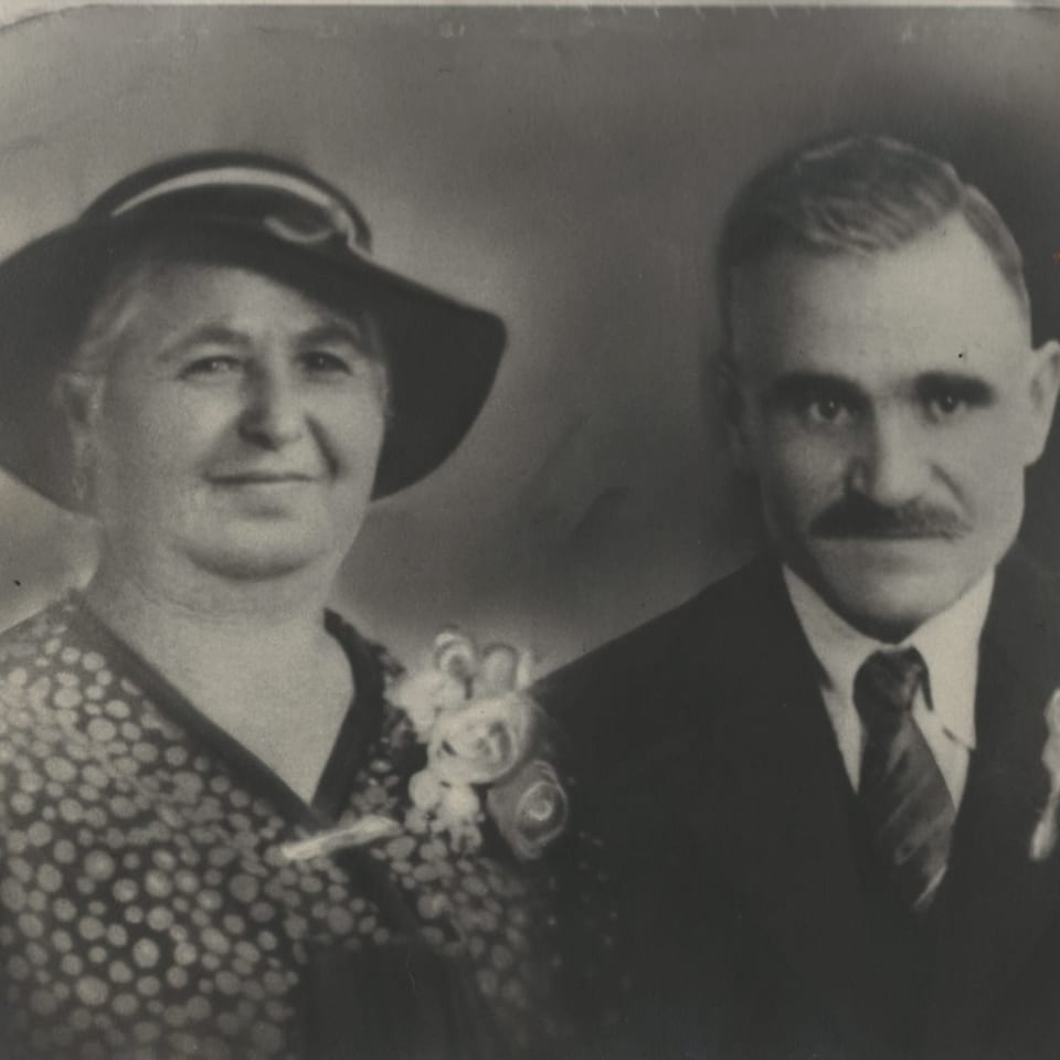 Black and white portrait of a smiling woman in a hat and a man in a suit.