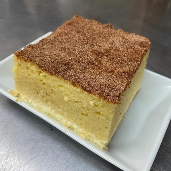 A square slice of light yellow cake, dusted with brown cinnamon sugar, on a white rectangular plate.