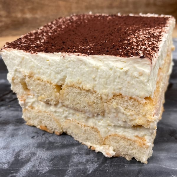 A close-up of a square slice of Rocco's Market & Deli tiramisu, topped with cocoa powder.