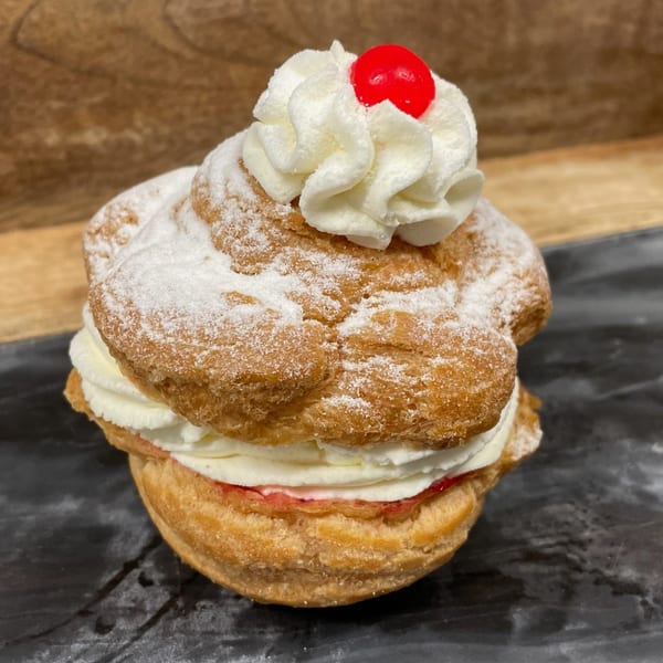 A cream puff with powdered sugar, whipped cream, and a red cherry on top.