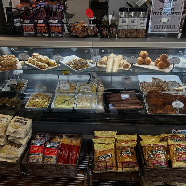 A deli display case at Rocco's Market & Deli filled with various prepared foods and packaged goods.