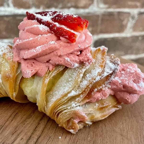 Flaky pastry filled with pink cream, topped with sliced strawberries and powdered sugar.