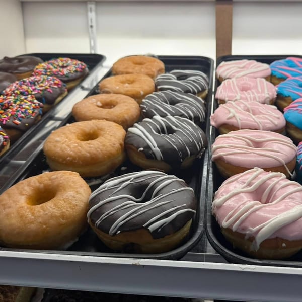 Trays of Rocco's Market & Deli donuts with various colorful frostings and sprinkles.