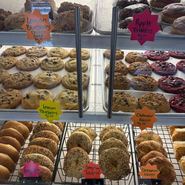 A deli display case filled with various baked goods, including cookies, bagels, and crumb cakes.