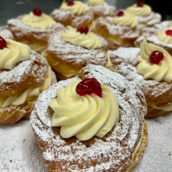 Close-up of Rocco's Market & Deli cream puffs, dusted with powdered sugar and topped with a cherry.