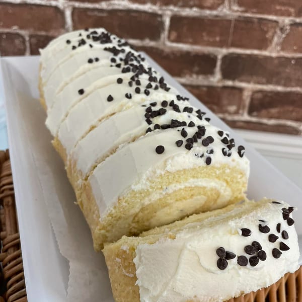 Sliced vanilla cake roll with white frosting and chocolate chips on a white platter.