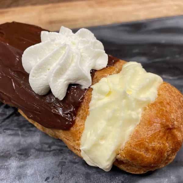 A Rocco's Market & Deli eclair with chocolate frosting, whipped cream, and vanilla cream filling.