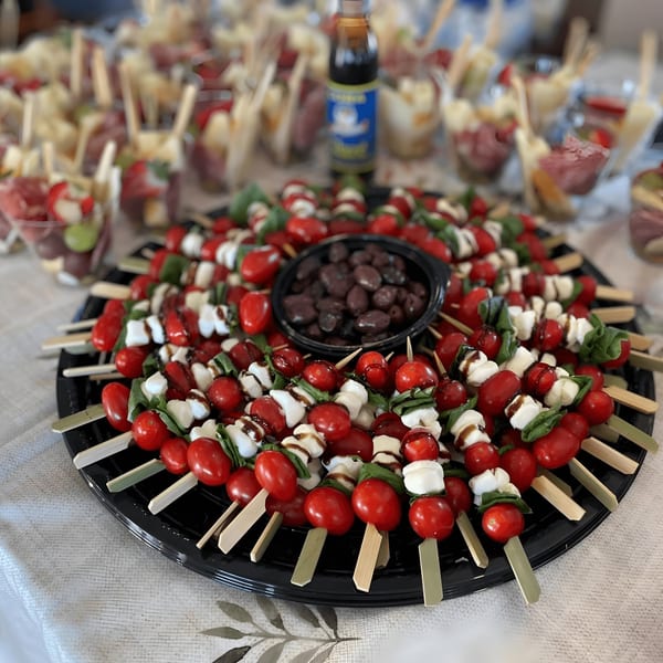 Caprese skewers with cherry tomatoes, mozzarella, basil, and balsamic glaze, alongside a bowl of olives.