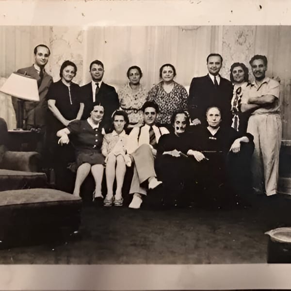 Black and white photo of a large family group, some seated and some standing, in a room.
