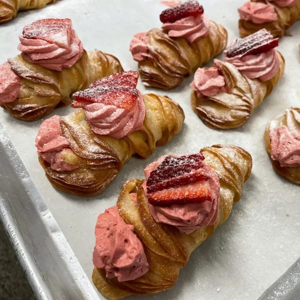 Several golden, flaky pastries with pink cream and sliced strawberries, dusted with powdered sugar.