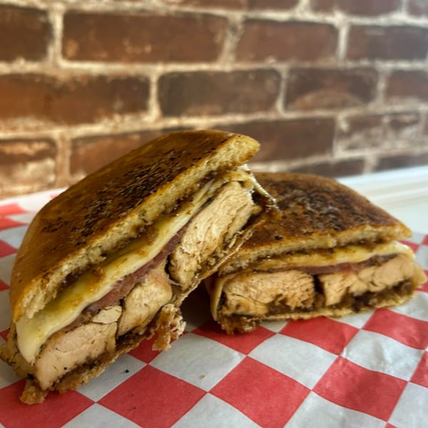 A grilled chicken panini, cut in half, sits on red and white checkered paper.