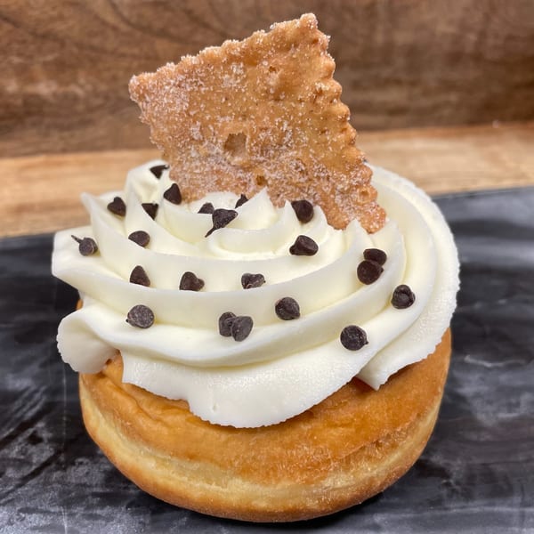 A Rocco's Market & Deli donut with white frosting, chocolate chips, and a churro piece.