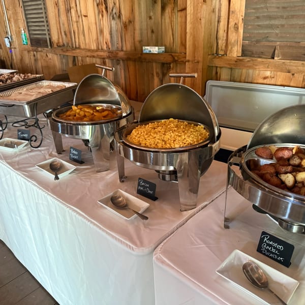 A buffet line with chafing dishes of baked peaches, bacon mac and cheese, and roasted garlic potatoes.