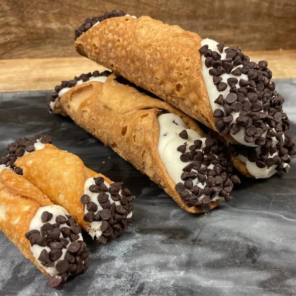 Three Rocco's Market & Deli cannolis filled with cream and topped with chocolate chips on a dark surface.