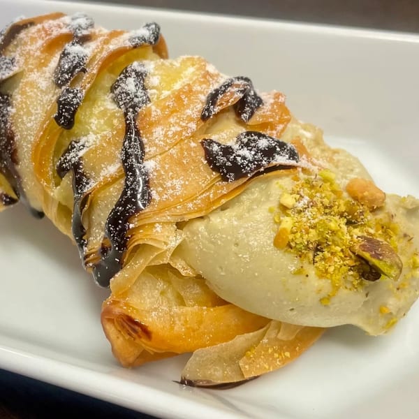 A Rocco's Market & Deli pastry with chocolate drizzle, powdered sugar, and pistachio cream.