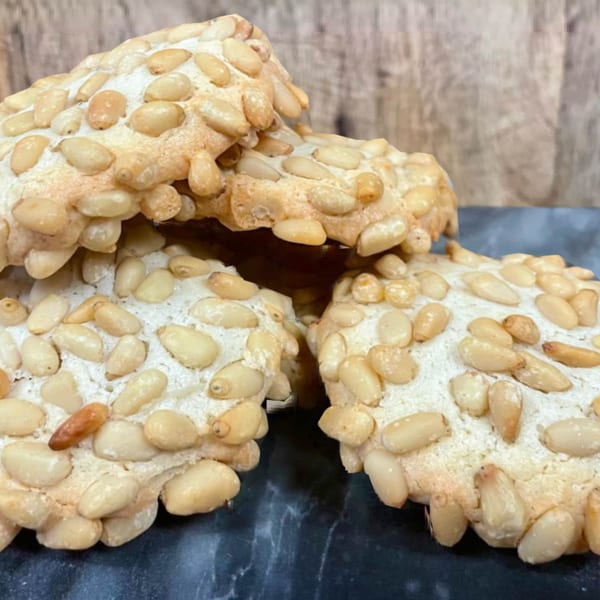 Close-up of Rocco's Market & Deli pine nut cookies, golden brown with a dusting of powdered sugar.