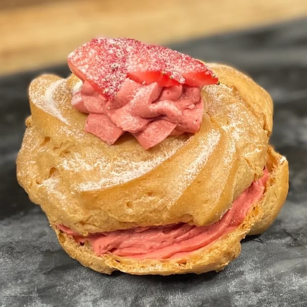 A golden choux pastry filled with pink cream, topped with a strawberry slice and powdered sugar.