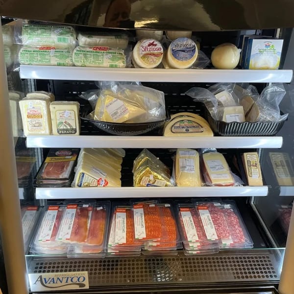 A refrigerated deli case at Rocco's Market & Deli filled with various cheeses and packaged meats.
