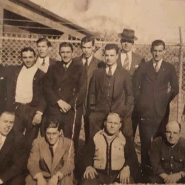 Vintage sepia photo of a group of men in suits and work clothes, likely Rocco's Market & Deli staff.