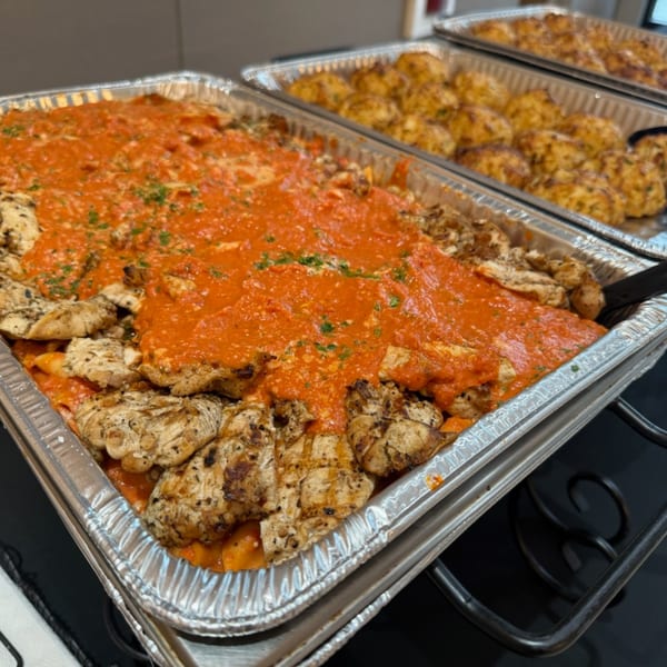 Two foil pans of deli food, one with grilled chicken and red sauce, the other with golden-brown items.