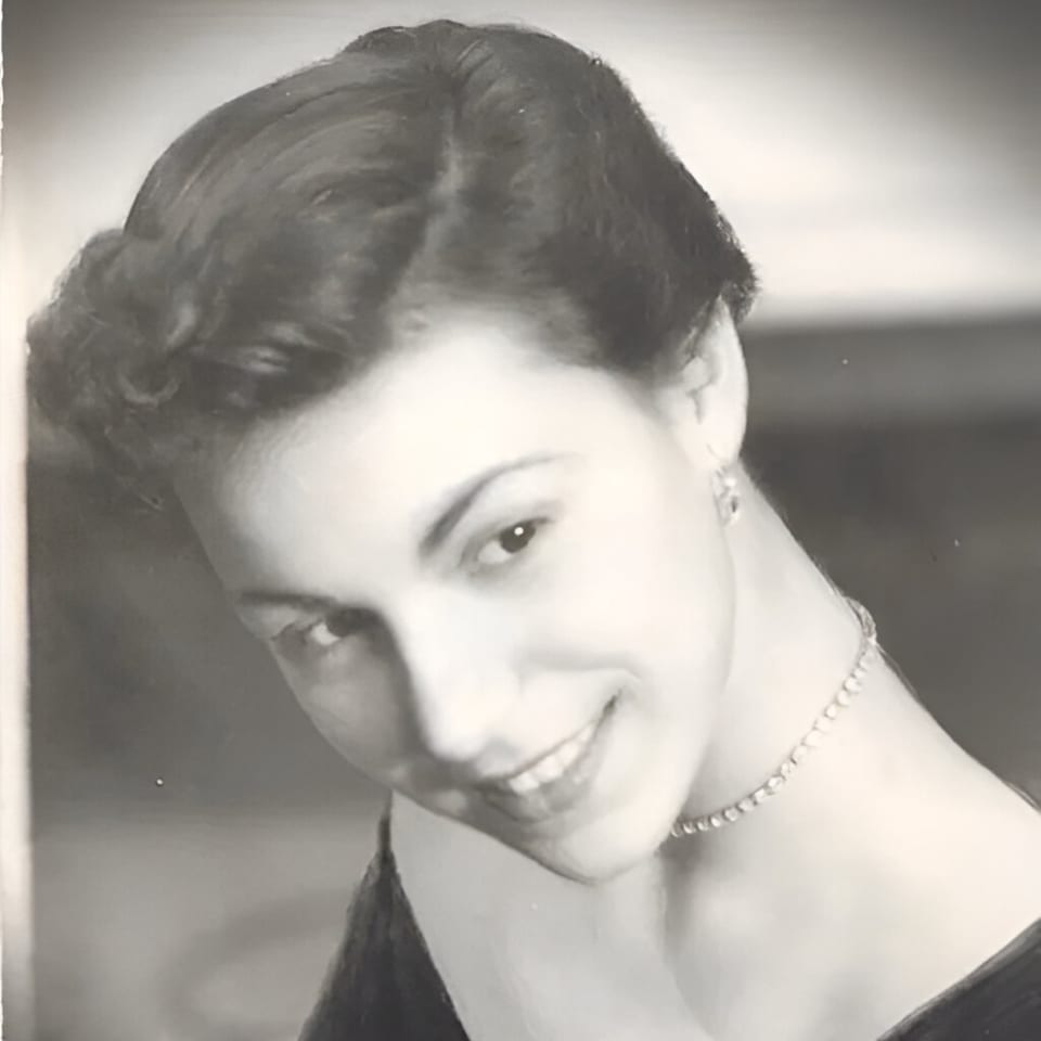 Black and white portrait of a smiling young woman with dark hair and a pearl necklace.