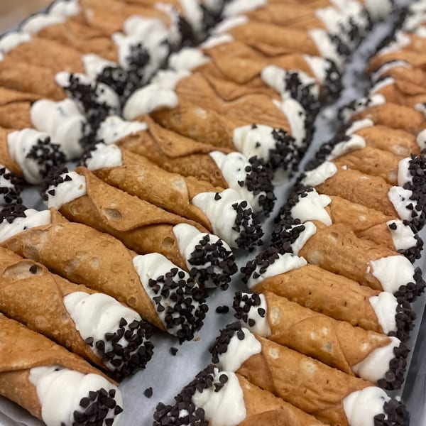 Rows of Rocco's Market & Deli cannolis with white cream and chocolate chips.