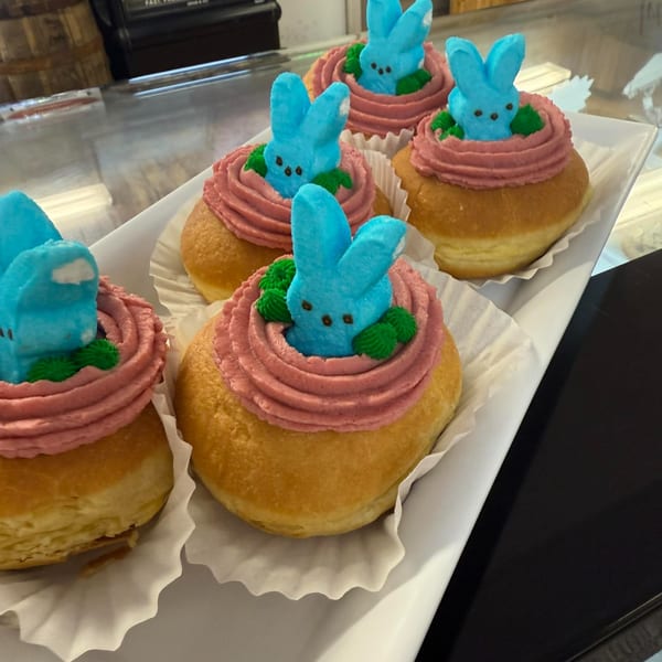 Five Rocco's Market & Deli donuts with pink frosting and blue Peeps bunnies on a white tray.